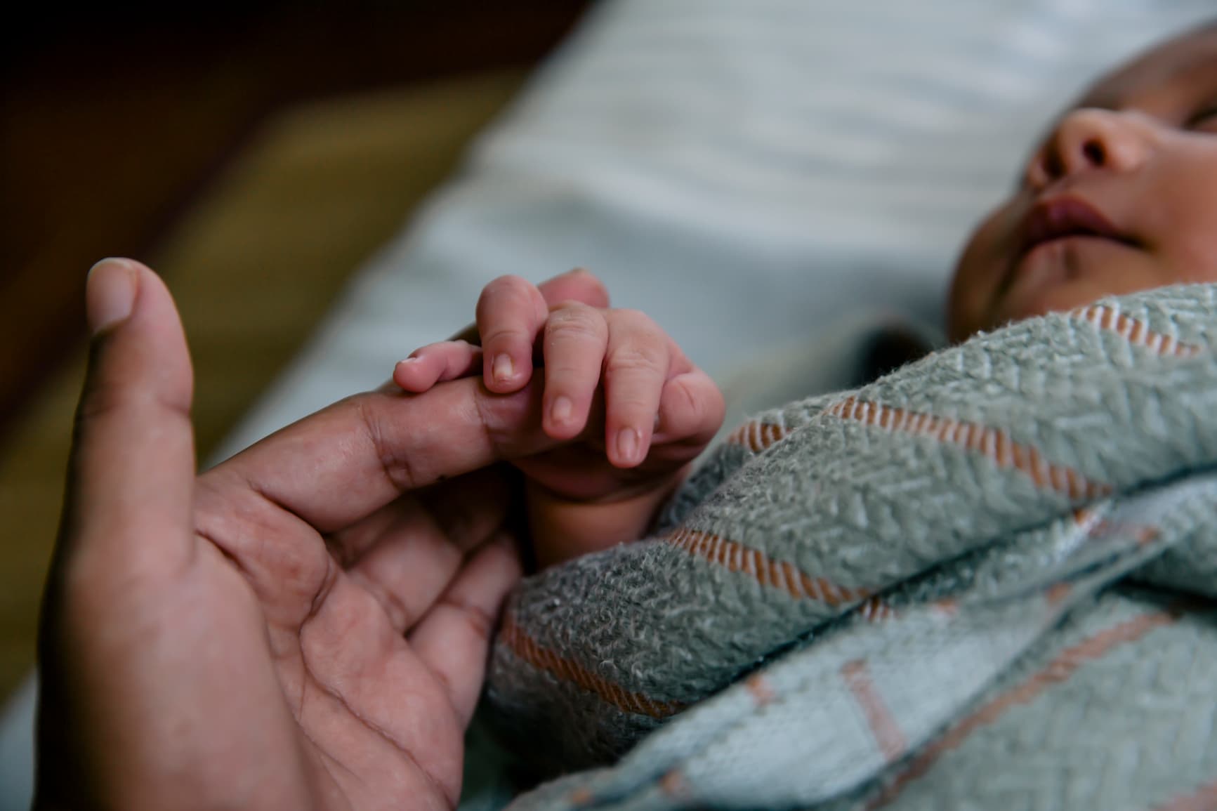 Close-up of a newborn baby grasping an adult’s finger, symbolising care, bonding, and early human connection.