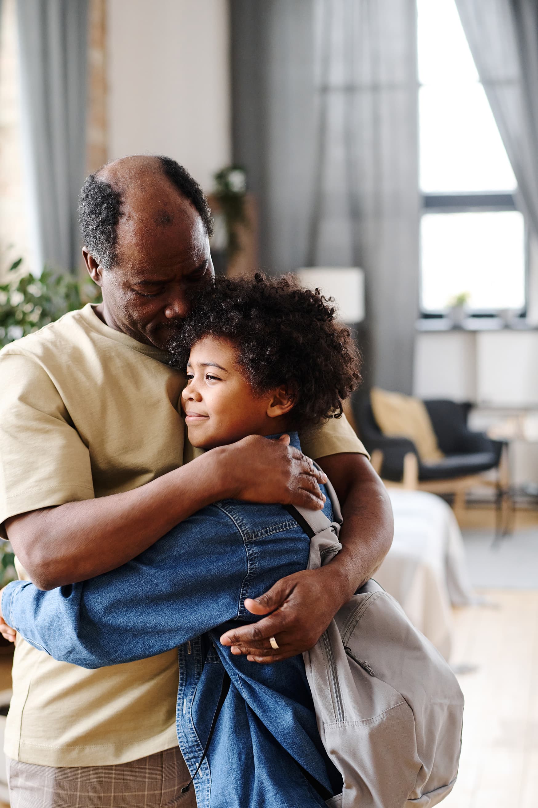 Older adult warmly hugging a young child indoors, conveying emotional support, family bonding, and intergenerational care in a home setting.