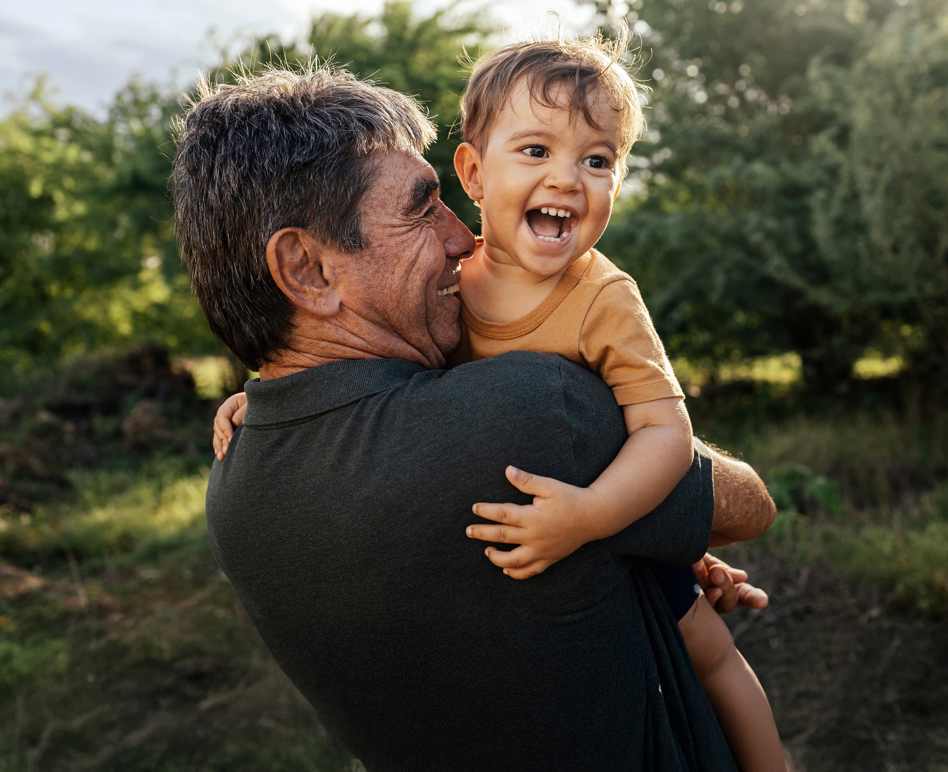 Older adult holding a laughing toddler outdoors in natural light, capturing joy, family bonding, and multigenerational connection.
